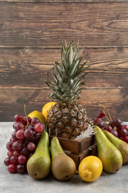 大理石の表面にさまざまな新鮮な果物が入った木製の箱に入った熟したパイナップル。