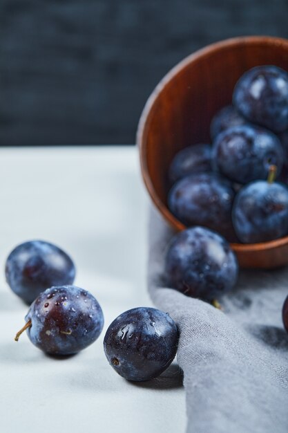Ripe plums in a bowl with gray tablecloth on white table.