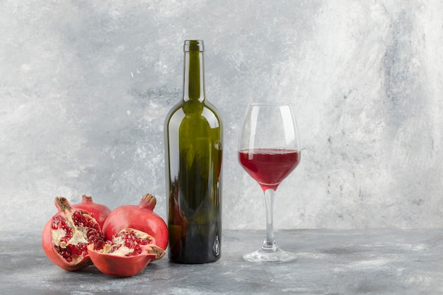 Ripe pomegranate fruits with a glass of wine on marble background.