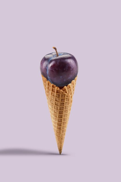 Ripe purple plum in a sweet wafer cone against lilac background. Concept of healthy nutrition, food and seasonal harvest of fruits. Close up, copy space