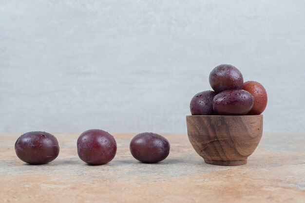 Ripe purple plums in bowl on marble background. 