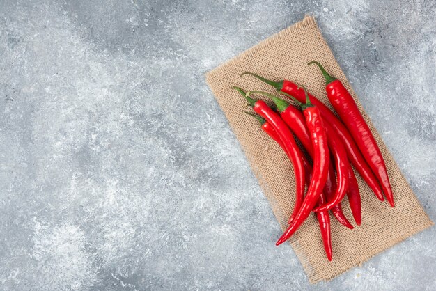 Ripe red chili peppers with sackcloth on marble surface.