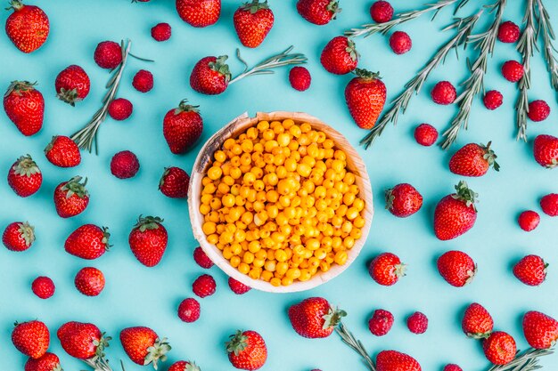 Ripe sea-buckthorn berries; strawberries and rosemary against blue background