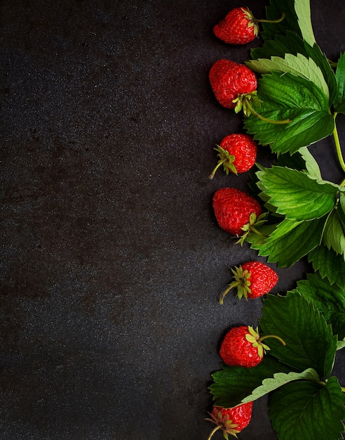 Ripe strawberries and leaves on black background. Top view