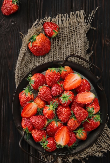Ripe strawberries in a metal dish on an old wooden background with copy space Viewpoint from above vertical frame Delicious natural dessert seasonal food