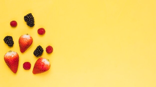 Ripe strawberry blackberry and raspberry on yellow background