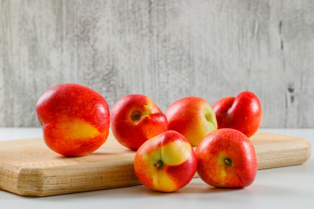 Ripe tasty peaches in a cutting board on white and grungy wall , side view.