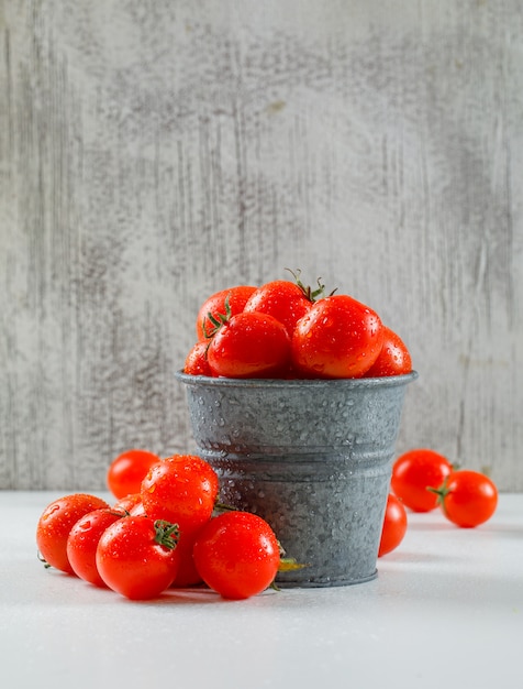 Foto gratuita pomodori bagnati maturi in un mini backet su una parete grungy e su una superficie bianca. vista laterale.