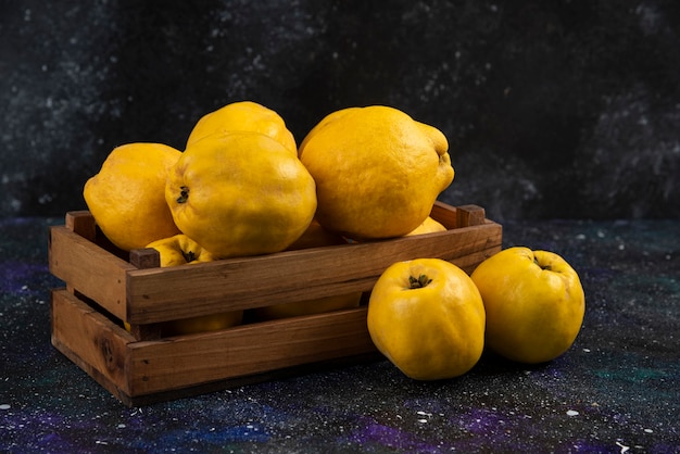 Free photo ripe whole quince fruits in wooden box on dark table.