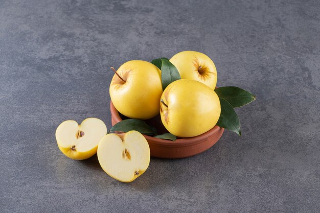 Ripe yellow apples with green leaves in clay bowl.