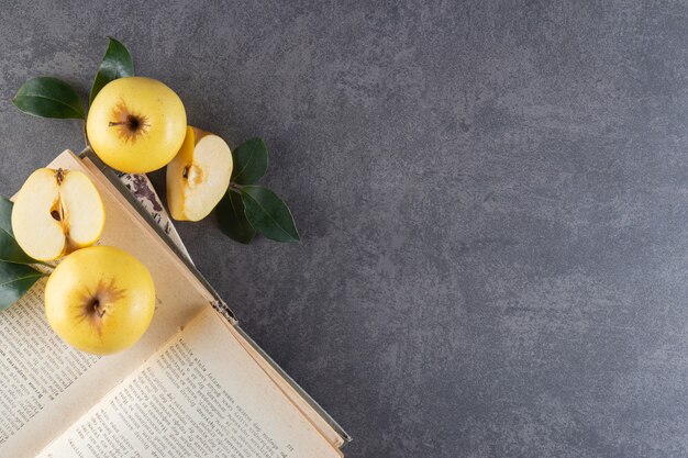 Ripe yellow apples with green leaves on top of book. 