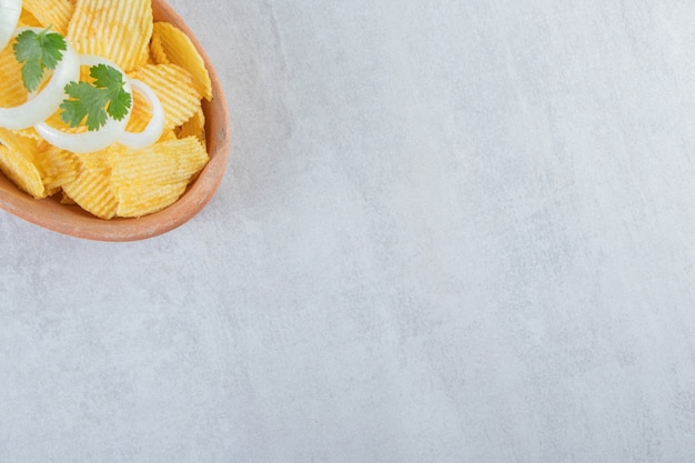 Rippled chips decorated with onion rings in ceramic plate.