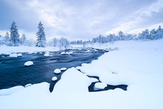 スウェーデンの冬は雪が積もった川と近くの森が雪に覆われています