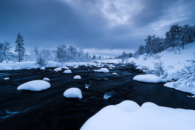 スウェーデンの冬は雪が積もった川と近くの森が雪に覆われています