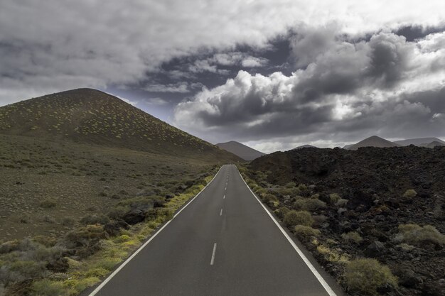 스페인 Timanfaya 국립 공원의 흐린 하늘 아래 언덕으로 둘러싸인 도로