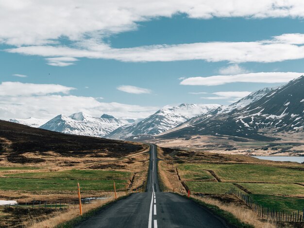 Road surrounded by hills covered in greenery and snow under a cloudy sky in Iceland