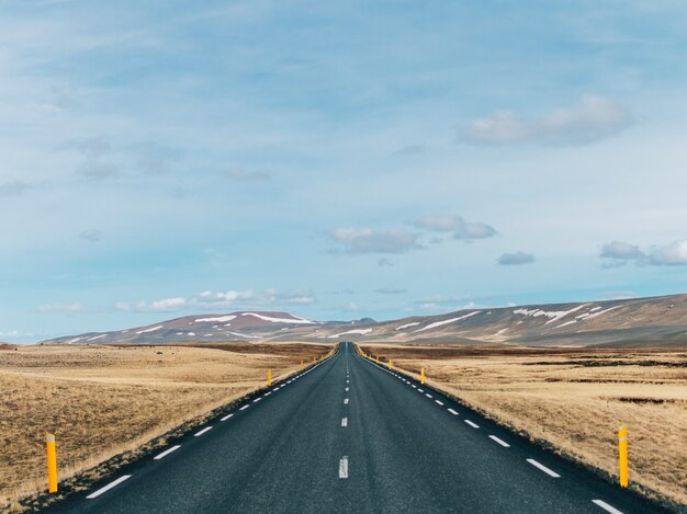 Road surrounded by hills covered in greenery and snow under a cloudy sky in Iceland