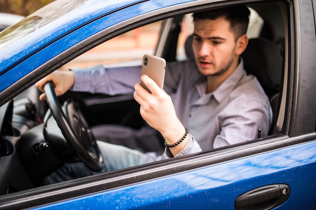 Road trip, transport, travel, technology and people concept. Happy smiling man with smartphone driving in car and taking photo on phone