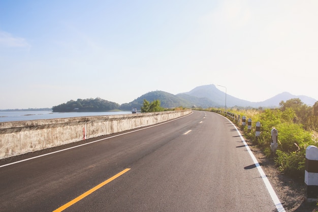 雲と青空の下で丘の緑の草の上の道。田舎道.Upの丘道.Vintage road。環境の道。自然の道.Asphalt road。青空、雲、道。田舎の道路。ストレートロード。ロードビュー。