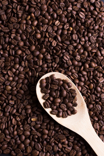 Roasted beans of tasteful coffee top view with wooden spoon