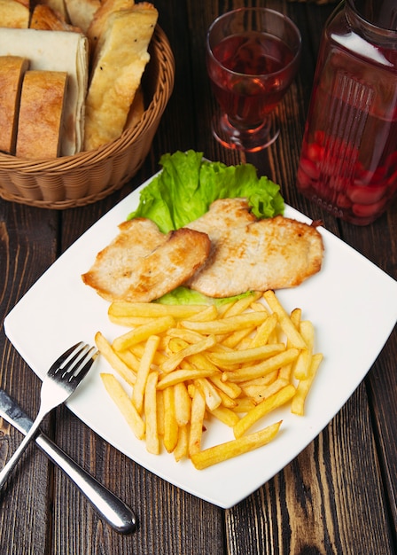 Roasted chicken breast nuggets with french fries in white plate.