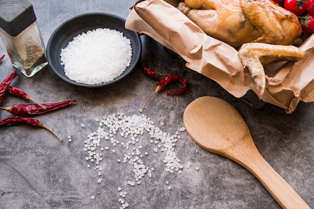 Roasted chicken in brown paper with ingredients on concrete background