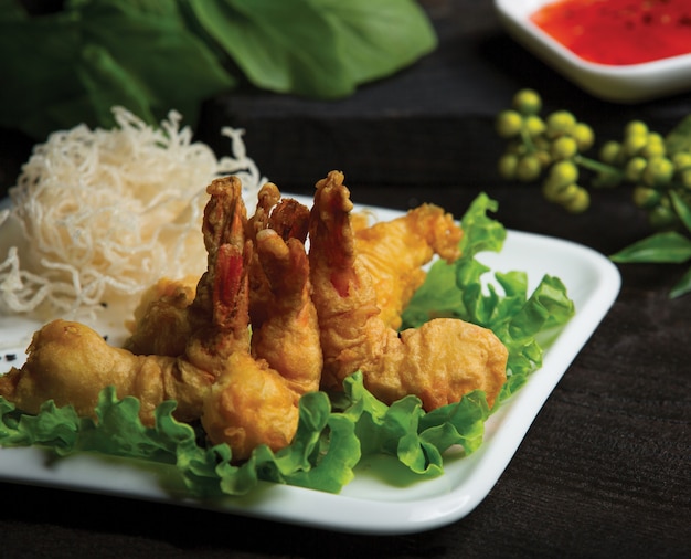 Жареные куриные ножки подаются с рисовыми спагетти и зеленым салатом в белой тарелке