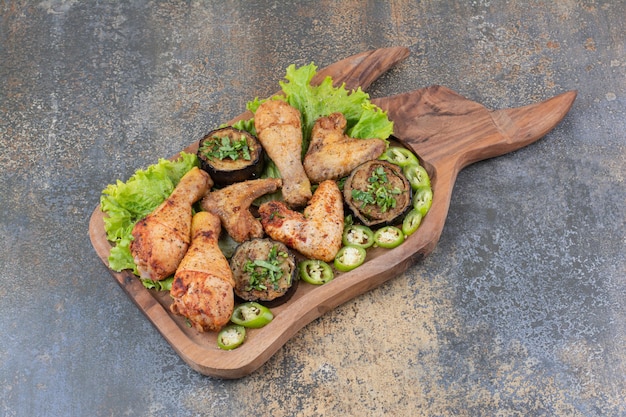 Жареные куриные ножки и крылышки на деревянной доске с салатом и перцем. Фото высокого качества