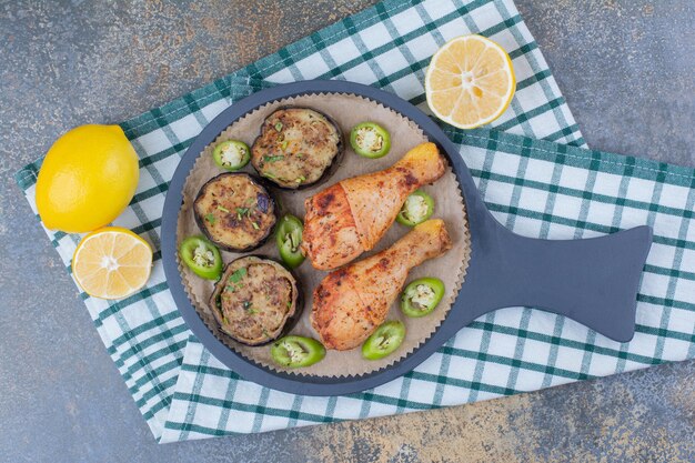 ダークボードに揚げ野菜とレモンを添えたローストチキンの脚。高品質の写真