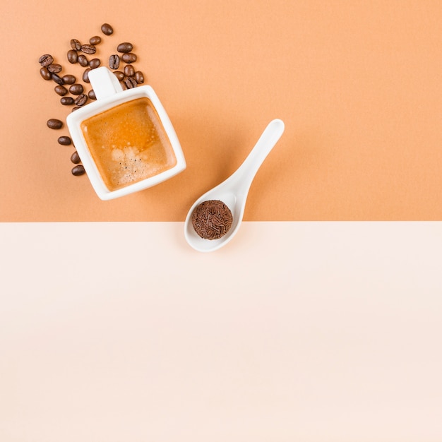 Foto gratuita chicchi di caffè tostati; tazza di caffè e palla di cioccolato nel cucchiaio sul doppio sfondo beige