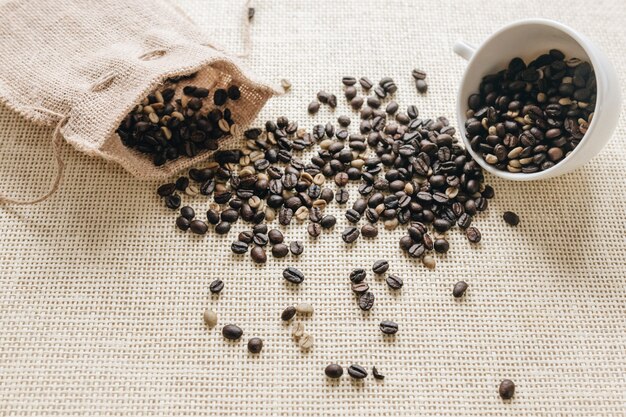 Roasted coffee beans falling from sack and ceramic cup