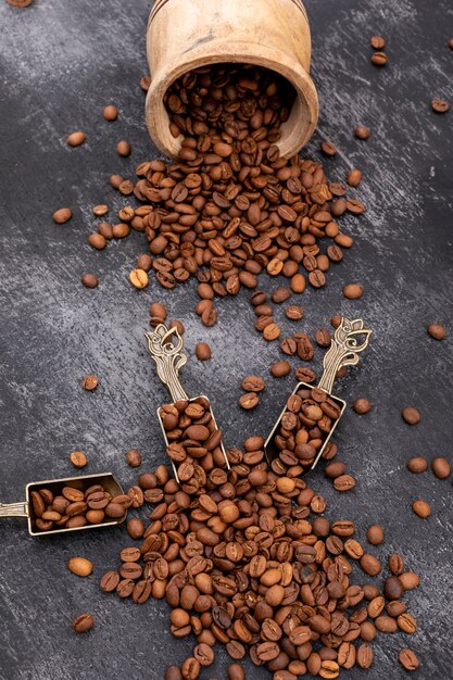 Roasted coffee beans in metal spoon on black surface