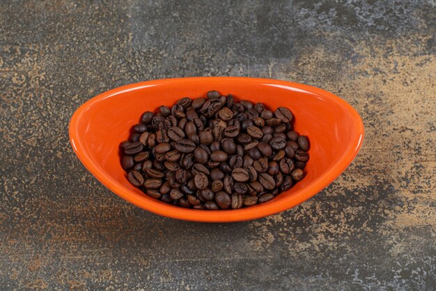 Roasted coffee beans in orange bowl.