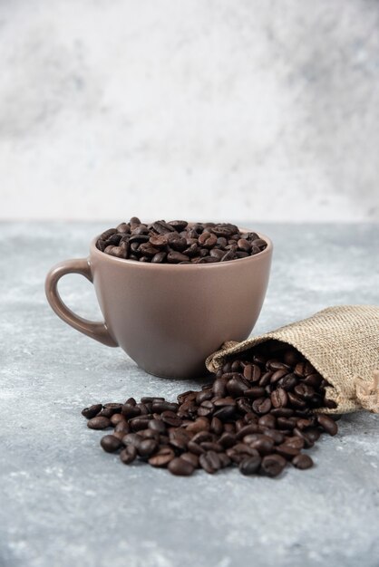 Roasted coffee beans out of burlap sack and in cup on marble.