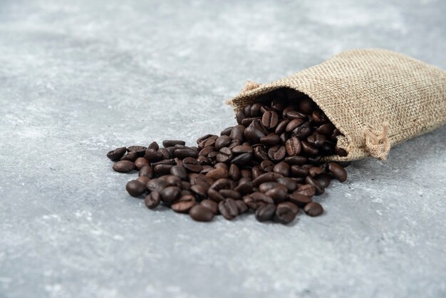 Roasted coffee beans out of burlap sack on marble.