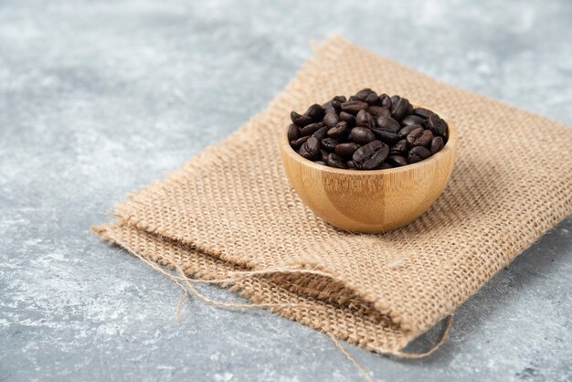 Roasted coffee beans in wooden bowl on marble.