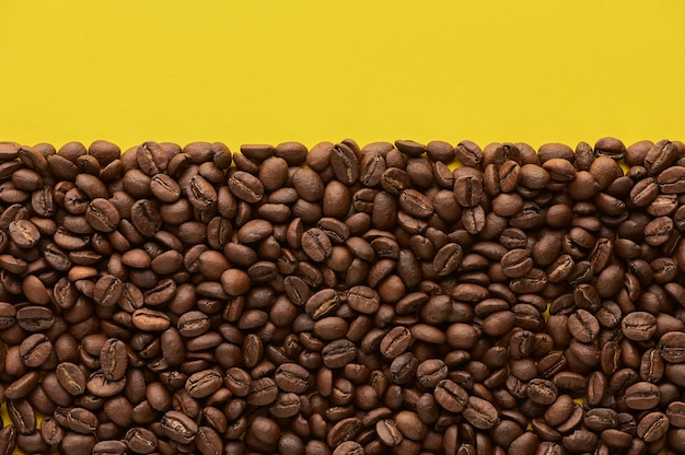 Roasted coffee beans on yellow background with copy space close up top view