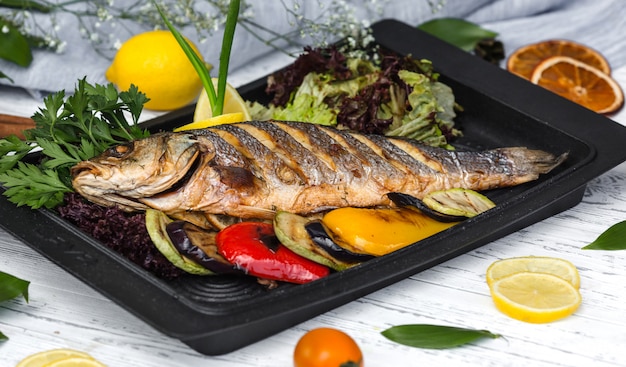 Roasted fish garnished with lemon slices served with vegetables