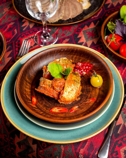 Free photo roasted fish in tomato sauce served with pomegranate seeds, cherry tomato and pepper slices