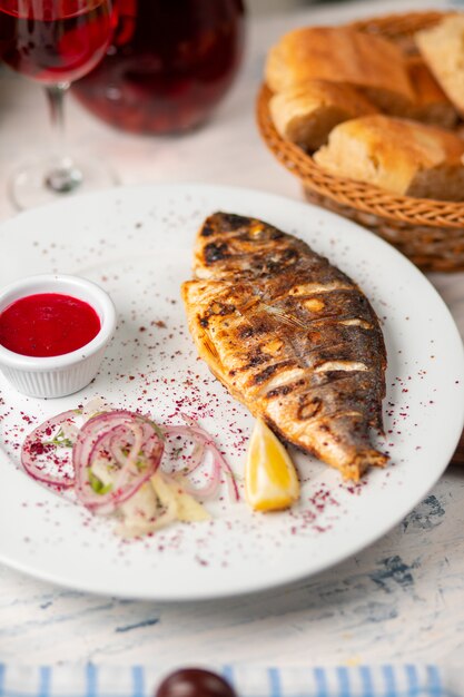 Roasted grilled fish served with herbs, lemon,  onion salad and dip red tomato sauce.