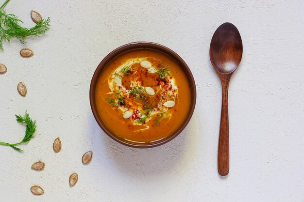 Roasted pumpkin and carrot soup with cream, black pepper and pumpkin seeds, cutting board and fresh pumpkin slices, black bread