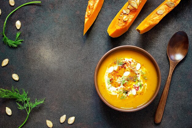 Roasted pumpkin and carrot soup with cream, seeds and fresh green in ceramic bowl. Top view