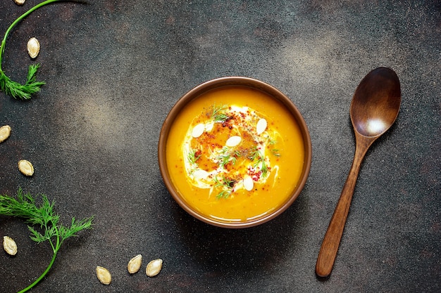 Жареный суп из тыквы и моркови со сливками, семенами и свежей зеленью в керамической миске. Вид сверху