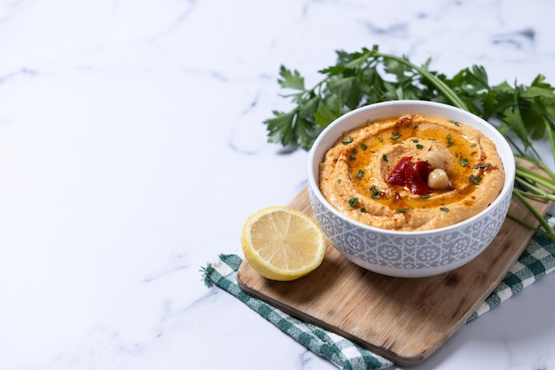 Free photo roasted red pepper hummus in white bowl on white marble background