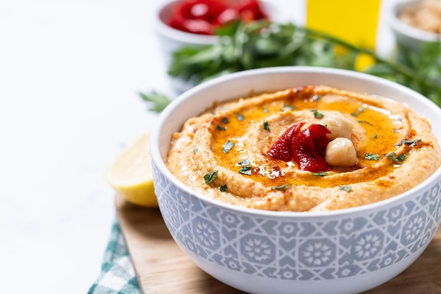 Free photo roasted red pepper hummus in white bowl on white marble background