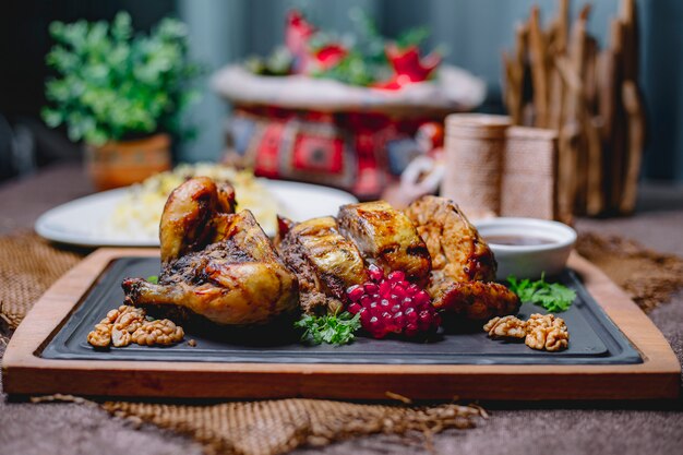 Жареная фаршированная курица, украшенная гранатом и грецкими орехами на черной доске и рисом в белой тарелке на деревянном столе