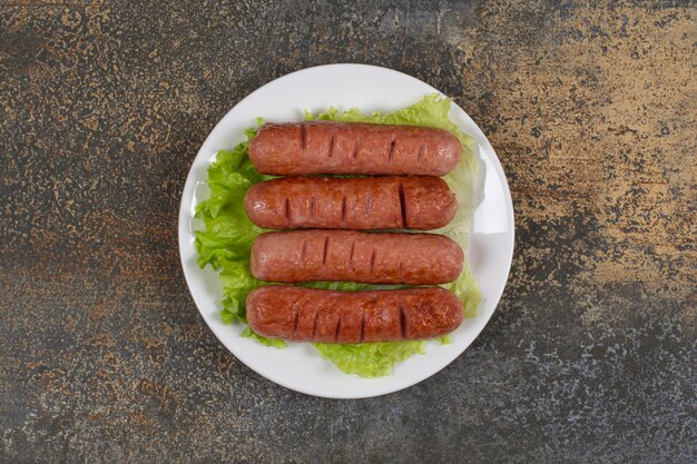 Roasted tasty sausages with lettuce on white plate.