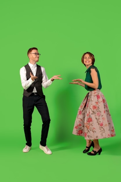 Rock n roll. Old-school fashioned young woman dancing isolated on green studio background. Young stylish man and woman.