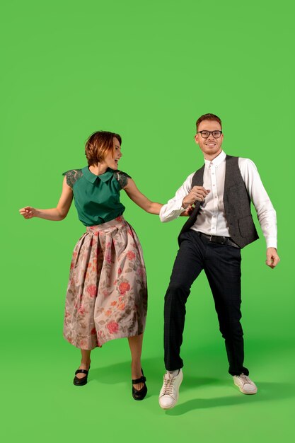 Rock n roll. Old-school fashioned young woman dancing isolated on green studio background. Young stylish man and woman.