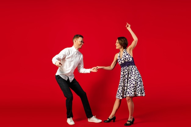 Rock n roll. Old-school fashioned young woman dancing isolated on red studio background. Young stylish man and woman.
